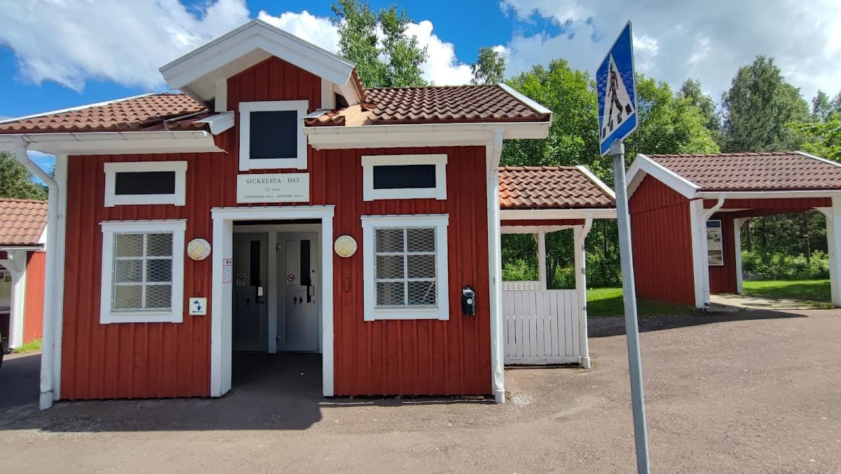 Rastplats Sickelsta V vid E20 med sittplatser, omgiven av öppna fält och grönskande lövskog.