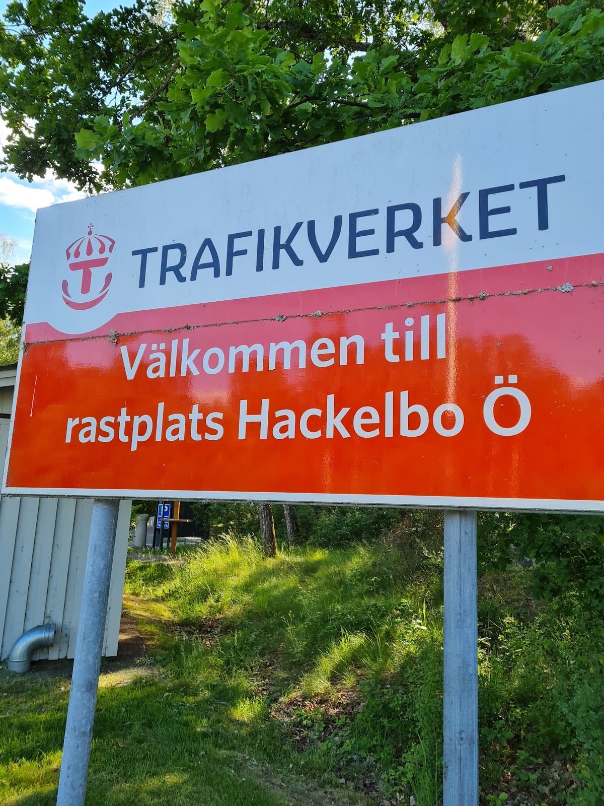 Vy över rastplats Hackelboö vid Testeboån med grönskande natur och sittplatser nära vattnet.