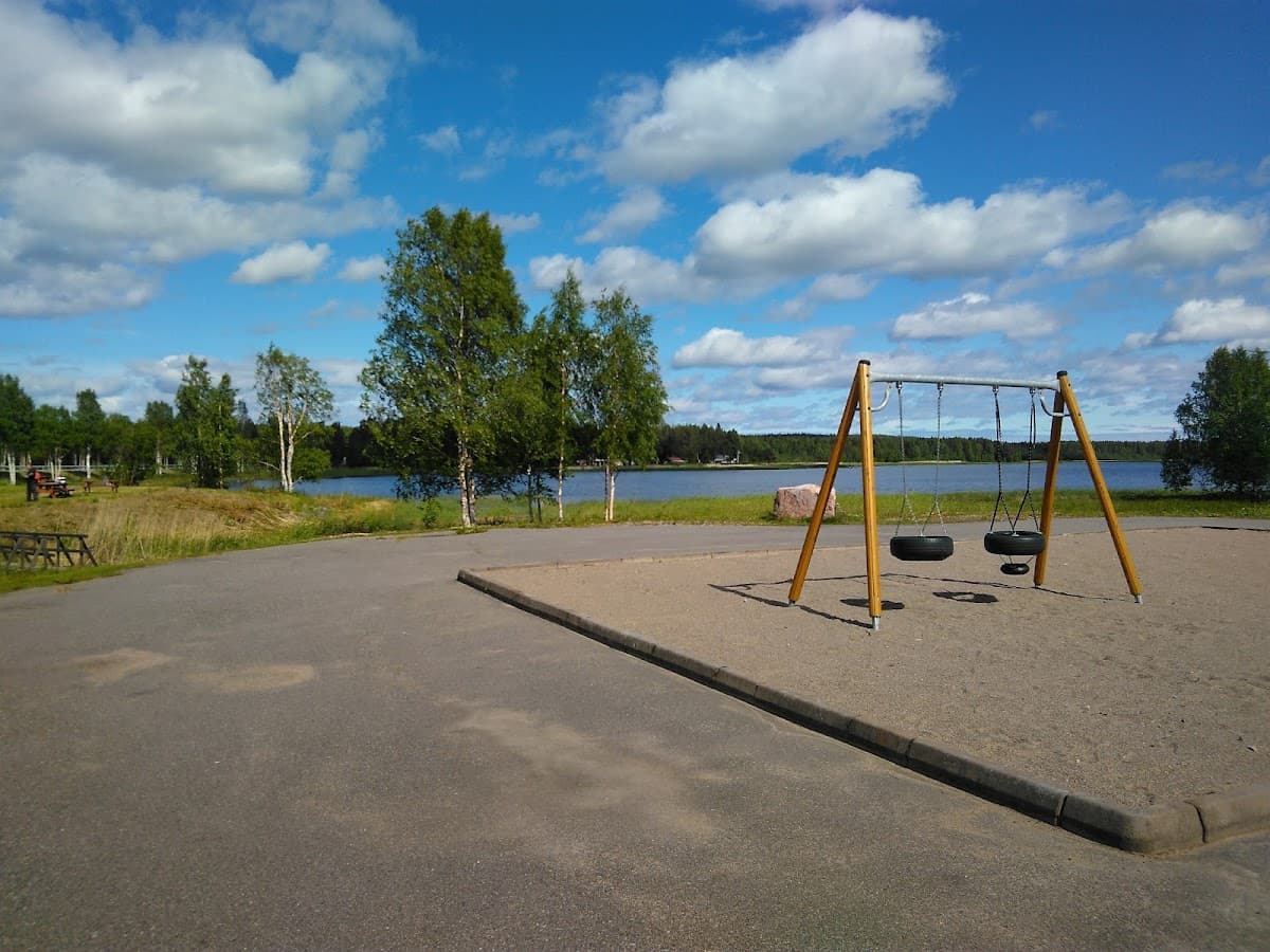 Rastplats Harrbäcken N vid E4, omgiven av skog med lekplats och servicebyggnad i bakgrunden.